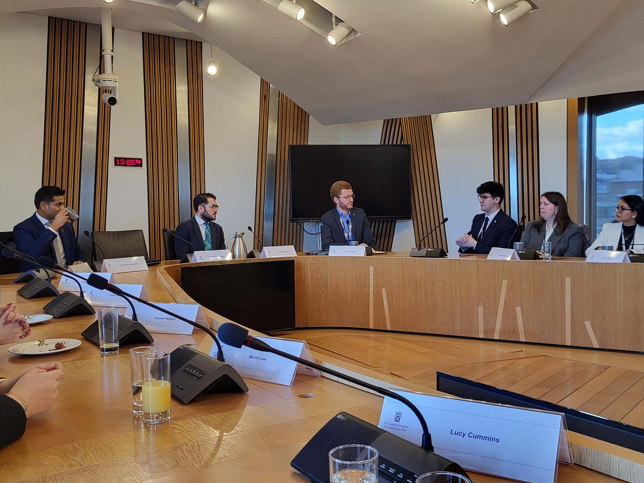 2025 Parliamentary Interns, Sandesh Gulhane MSP, Paul Sweeney MSP and Ross Greer MSP sat in a Committee Room in the Scottish Parliament Building.